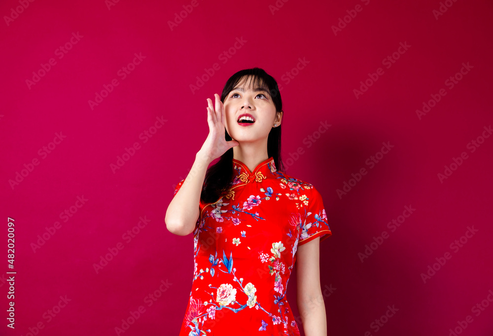 Smiling asian young woman in traditinal red cheongsam dress pointing hand to empty space on red background. Smiling asian young woman in traditinal red cheongsam dress pointing hand to empty space on red background.