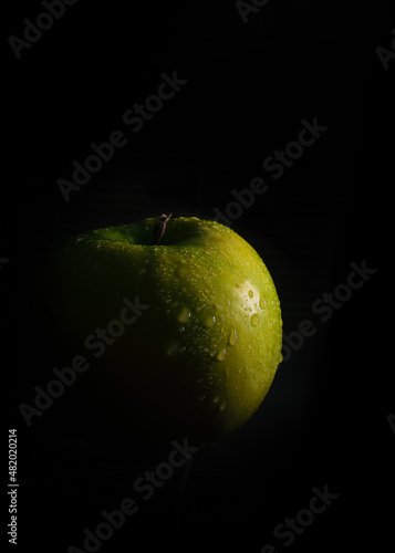 A green apple sitting in complete darkness with light shining on it from one side