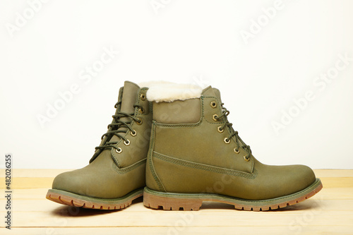 Leather green waterproof boots with white fur for winter hiking wooden table. Winter shoes. Warm shoes with fur. Fashion, trendy footwear. Close up view.