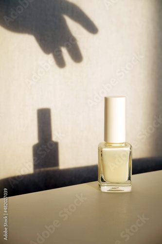 White nail polish or nail care product in glass bottle. Shadow of reaching hand