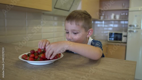 the boy is sitting at the table and eating strawberries