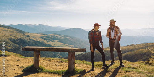 Fotografi Couple of hikers with backpacks enjoying valley landscape view from top of a mountain