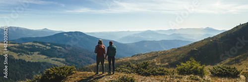 Photography Couple of hikers with backpacks enjoying valley landscape view from top of a mountain