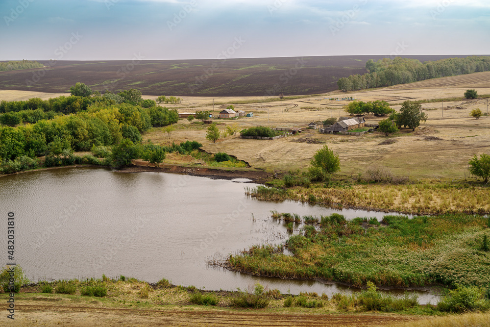Rural landscape with a village on the banks of a pond and fields. Russia, Orenburg region, farm Arapovka