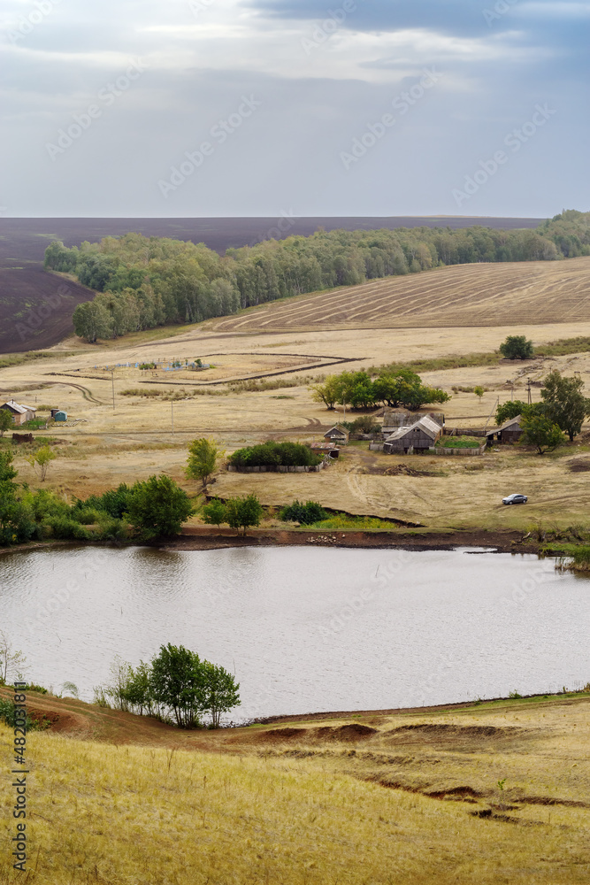 Rural summer landscape with a village near a pond, a cemetery and fields. Russia, Orenburg region, farm Arapovka