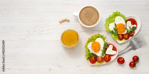 Festive breakfast for two persons on Valentines Day Two heart-shaped plates with fried eggs vegetables and cheese coffee and juice on a white wooden table with the word love laid out of letters Banner