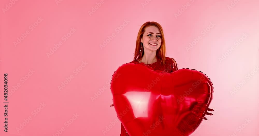 Beautiful redhead girl with red heart balloon posing. Happy Valentine's Day concept. Studio photo of beautiful ginger girl dancing on pink background. Beautiful redhead girl with red heart balloon posing. Happy Valentine's Day concept. Studio photo of beautiful ginger girl dancing on pink background.