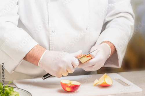 Unrecognizable chef in uniform cutting an apple on a plastic cutting board