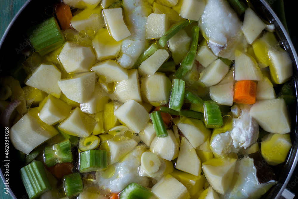 Boiled cod with potatoes, celery and carrots. Close-up of pan ready to cook, on green wooden background Boiled cod with potatoes, celery and carrots. Close-up of pan ready to cook, on green wooden background