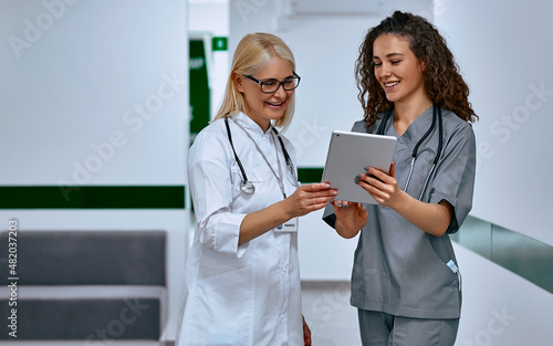 Doctors laugh and talk in the hallway. Older woman and young female doctors.