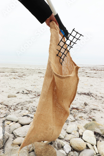 Collecting plastic waste on a beach with the sea in the background. Environmental protection on the beach. Collection of plastic waste in a hessian bag (France - 21/01/2022)