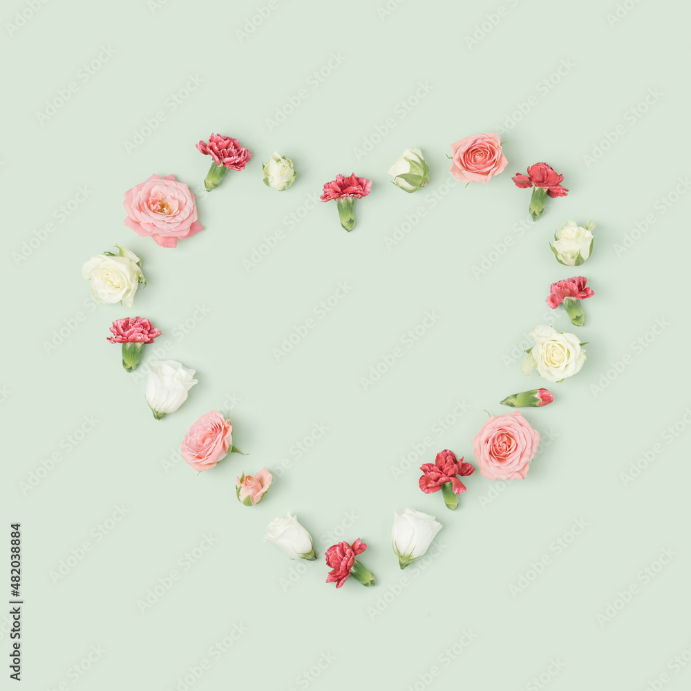 Various colorful spring flowers heart layout on a light green background. Valentine's day minimal concept.