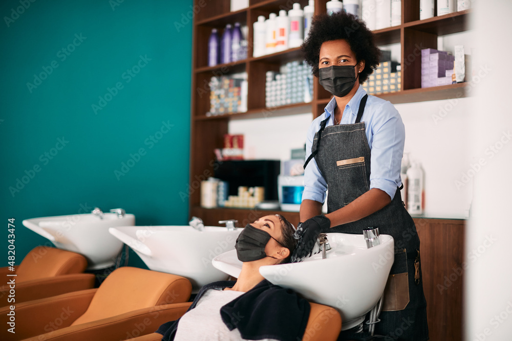 Black hairstylist washes woman's hair while working at hair salon