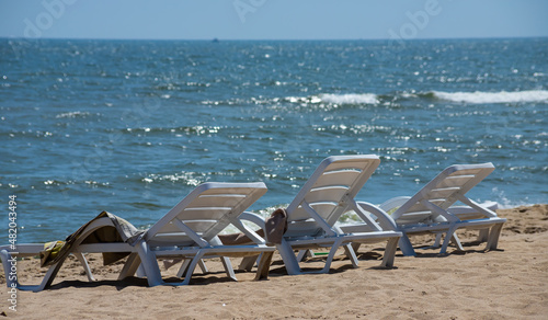 The seashore without people on a sunny summer vacation day. A white plastic sunbed stands on the white sand beach against the background of the sky and sea waves