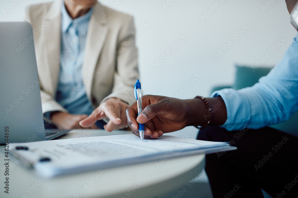 Close-up of black man signing contract with insurance agent in the office. - obrazy, fototapety, plakaty 