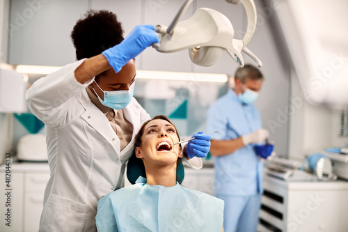 Black female dentist examining teeth of young woman at dental clinic.