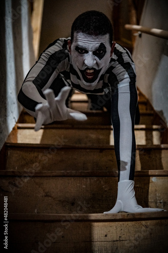 Vertical horrifying shot of a male in a mime costume posing with a scary expression on the stairs
