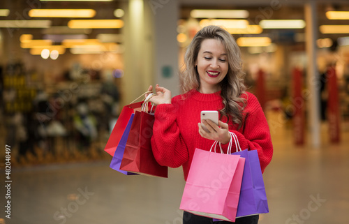a girl with blond hair in a mall with bright packages and a phone in her hands spends a day of shopping, shopping in the mall