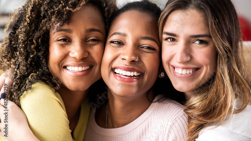 Three beautiful smiling girl friends hugging together - Multiracial group of women looking at camera - Females and happy lifestyle concept