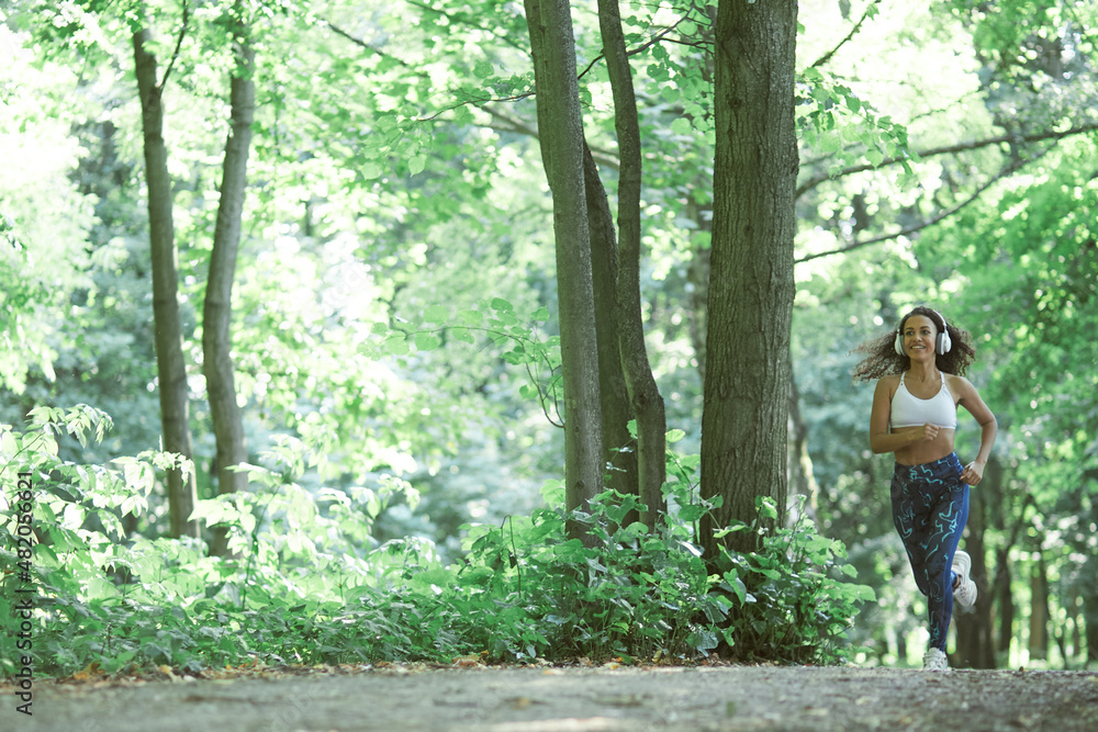 Beautiful young afro girl running in the park in summer listening to music with headphones Beautiful young afro girl running in the park in summer listening to music with headphones