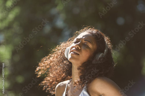 Excited girl dancing and listening music with headphones and smart phone in the park with hair moving