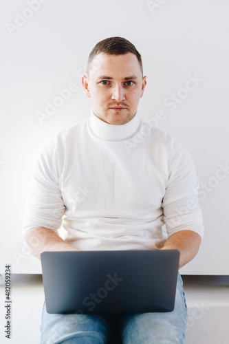 man working with laptop on knees in light room