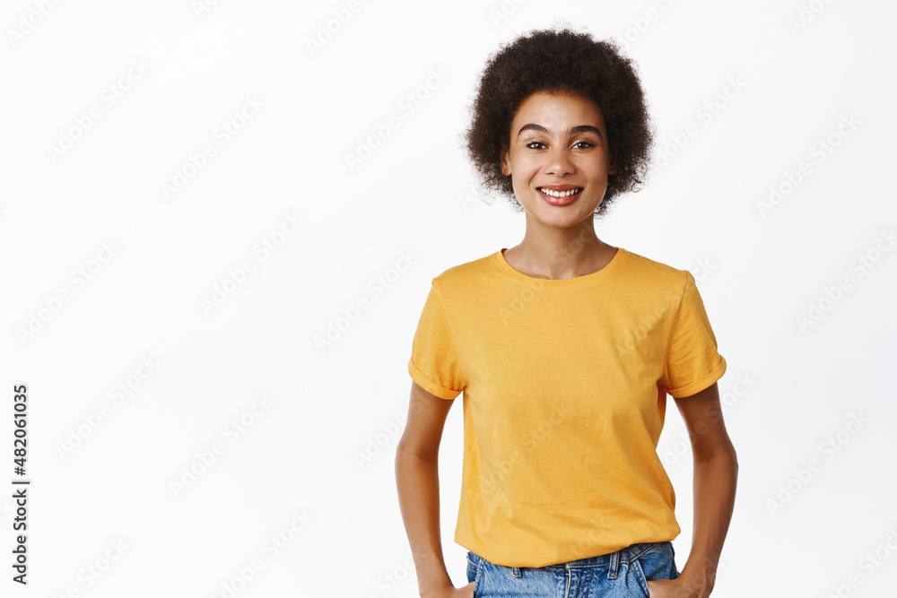 Smiling modern black girl in yellow t-shirt looking happy at camera, casual relaxed pose, white background Smiling modern black girl in yellow t-shirt looking happy at camera, casual relaxed pose, white background
