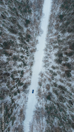 The car is driving through a snowy forest. Aerial photography