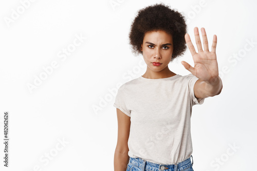 Stop. Serious frowning african woman extend arm, showing block, refusal gesture, prohibit, forbid smth, standing against white background