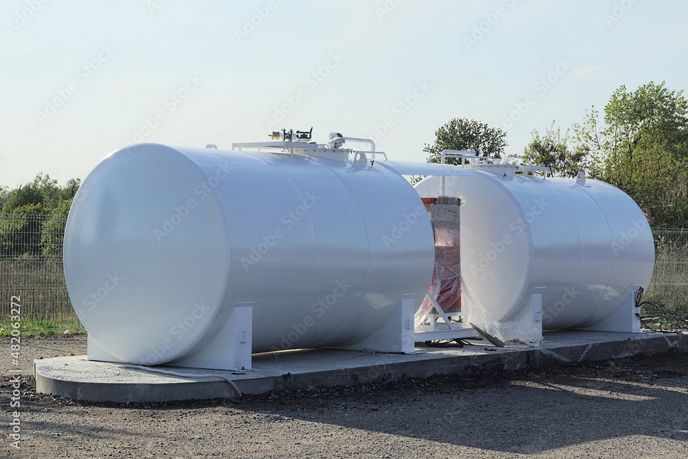 two big industrial metal white barrels at a gas station stand on gray asphalt by the road two big industrial metal white barrels at a gas station stand on gray asphalt by the road
