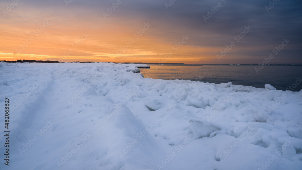 Bright orange winter sunset over the sea, beach covered with snow