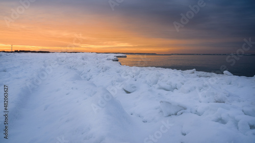 Bright orange winter sunset over the sea, beach covered with snow