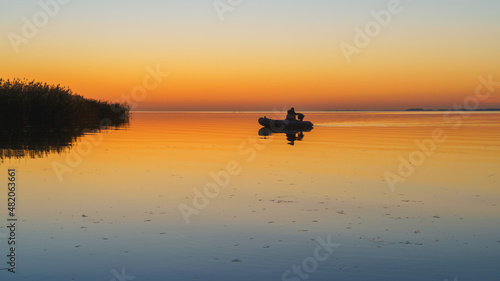 fisherman sails on a boat on a quiet lake, stunning sunset in the background
