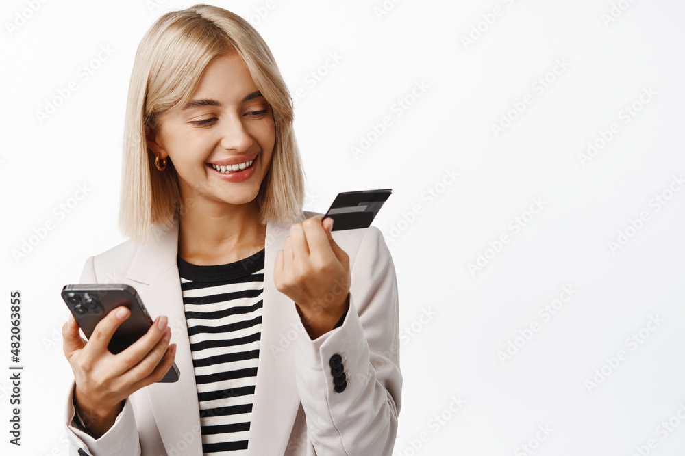 Portrait of young office woman, ceo manager in suit using credit card and mobile phone, buying online on smartphone app, making purchase, register her card, white background Portrait of young office woman, ceo manager in suit using credit card and mobile phone, buying online on smartphone app, making purchase, register her card, white background