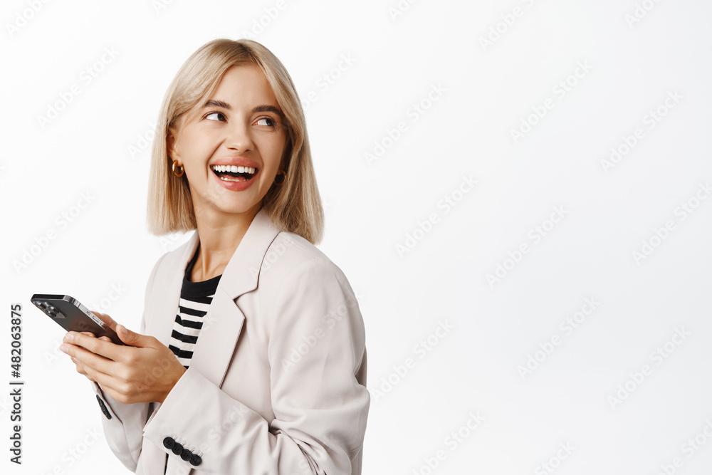 Happy successful businesswoman using mobile phone, looking away at copy space, company logo, standing in suit over white background and laughing Happy successful businesswoman using mobile phone, looking away at copy space, company logo, standing in suit over white background and laughing