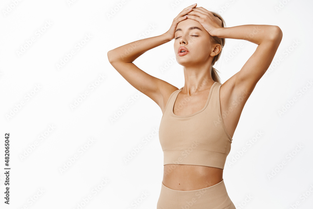 Fototapeta premium Portrait of female athlete, sporty girl sweating after workout, running, finish jogging, holdig hands on head and panting from sport exercises, white background