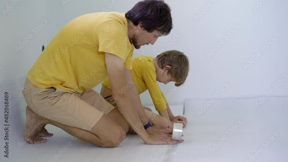 A father an son are laying out and glue the insulation for the floor, on which they will then lay the laminate A father an son are laying out and glue the insulation for the floor, on which they will then lay the laminate