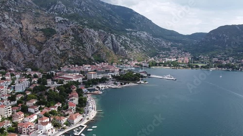 Smooth aerial of beautiful Kotor Old Town and marina bay shot with drone on summer day in Montenegro, view of historical architecture, tourist attractions, boats in harbor, people on beach park