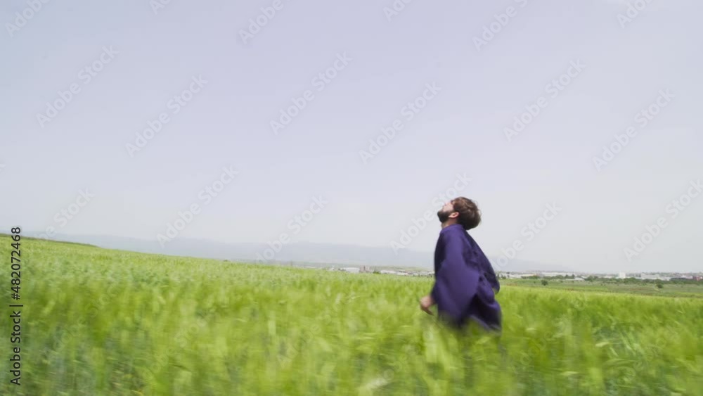 Young man with graduation clothes running in a green field throwing hat in the air.. Young man with graduation clothes running in a green field throwing hat in the air..