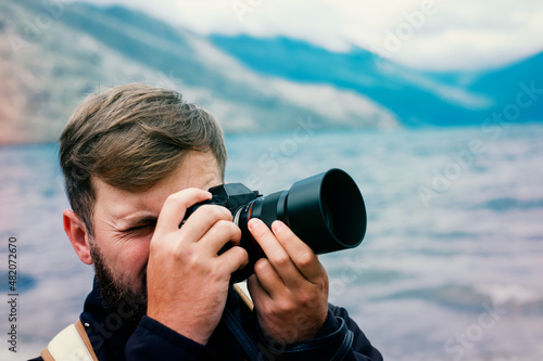 Portrait of a photographer taking a picture with his hand on the camera. Focusing and shooting a landscape in outdoor.
