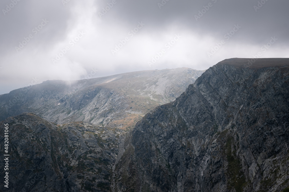 Dark, moody, cloudy sky and mist above impressive, rocky, pointy peaks of Rila mountain national park in Bulgaria