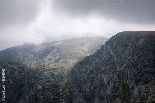Dark, moody, cloudy sky and mist above impressive, rocky, pointy peaks of Rila mountain national park in Bulgaria