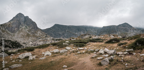 Panorama of impressive Rila mountain rocky, pointy peaks on a moody day with murky clouds and foreground rocks