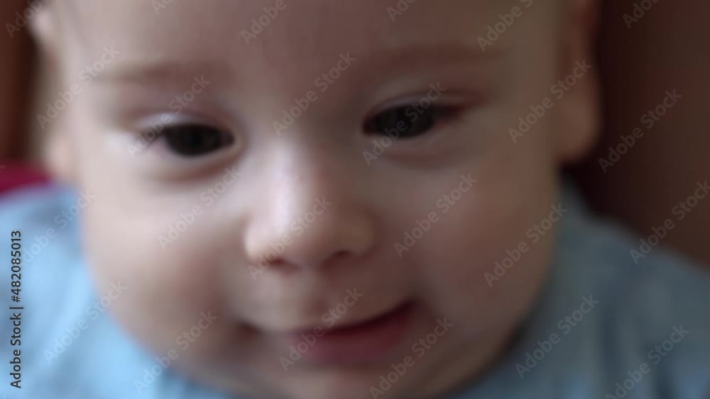 Close-up Smiling Face Of Newborn Baby In Early Days Wakes Up Opens Eyes. Infant Child Grimaces After Dream In Blue Bodysuit. Kid In First Minutes Of Life Portrait In Macro. Childhood, Infancy Concept Close-up Smiling Face Of Newborn Baby In Early Days Wakes Up Opens Eyes. Infant Child Grimaces After Dream In Blue Bodysuit. Kid In First Minutes Of Life Portrait In Macro. Childhood, Infancy Concept