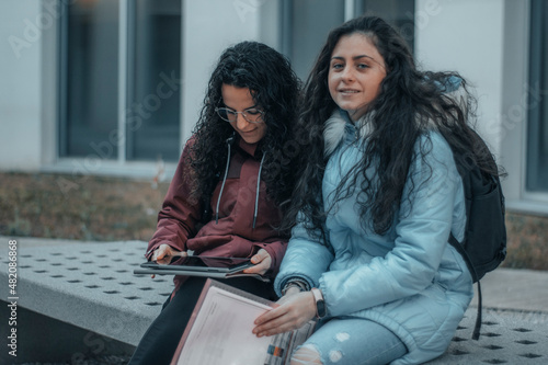 Chicas jovenes estudiantes sentadas en el campus universitario revisando sus tareas y apuntes escolares para estudiar en su hora de descanso