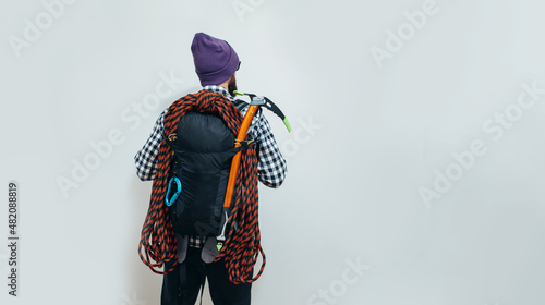Brutal bearded guy mountaineer with a tourist backpack, an ice ax and a rope is going on a journey. Studio shot photo