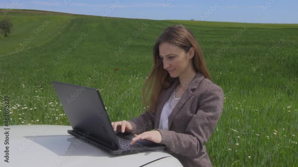 Bussinesswomanl with a laptop on a car, alone in a green field. Freedom, business, work from anywhere and social distancing concept. Bussinesswomanl with a laptop on a car, alone in a green field. Freedom, business, work from anywhere and social distancing concept.