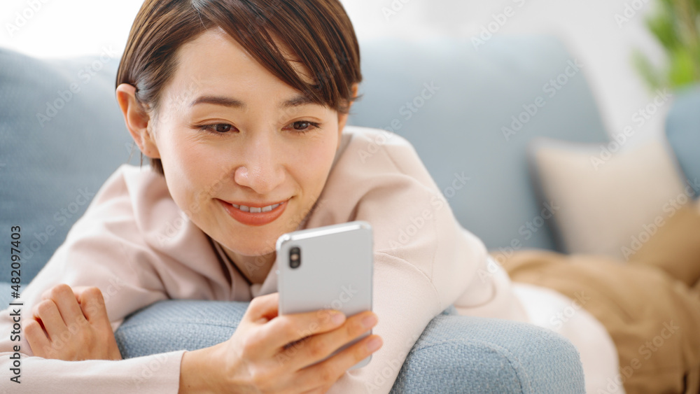 ソファーに寝転がりながらスマートフォンを使う女性 ソファーに寝転がりながらスマートフォンを使う女性
