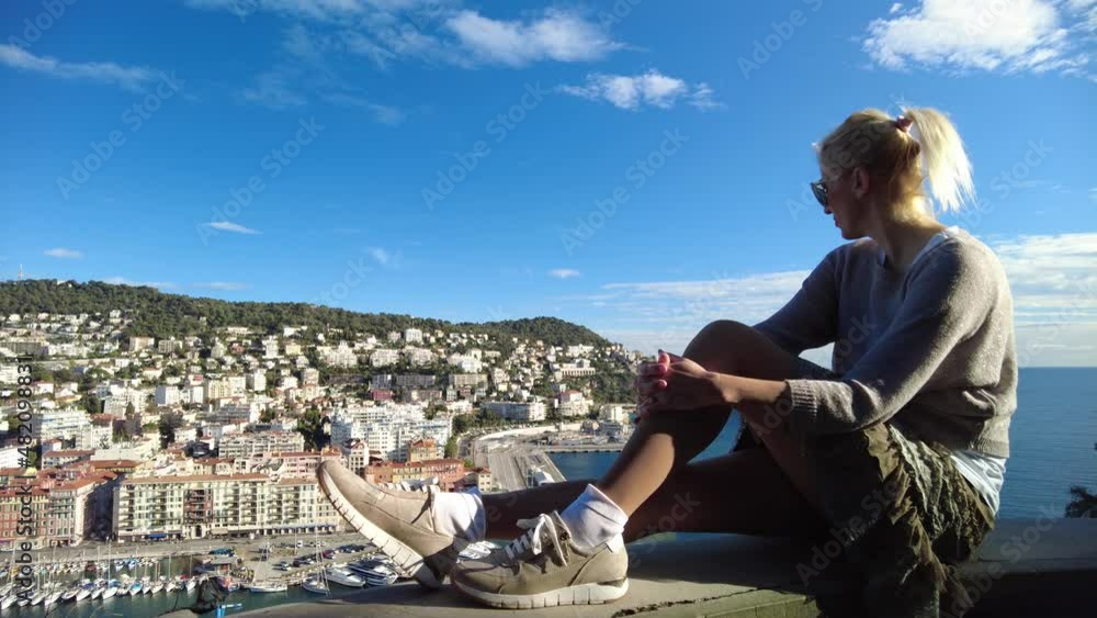 woman sitting on top rooftop view of panorama of the Nice city and Port Lympia in Blue Coast of France. Aerial view of cityscape with lighthouse from the panoramic terrace of Colline du Chateau park.