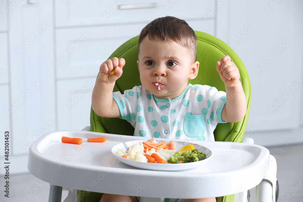 Cute little baby eating healthy food in high chair at home Cute little baby eating healthy food in high chair at home